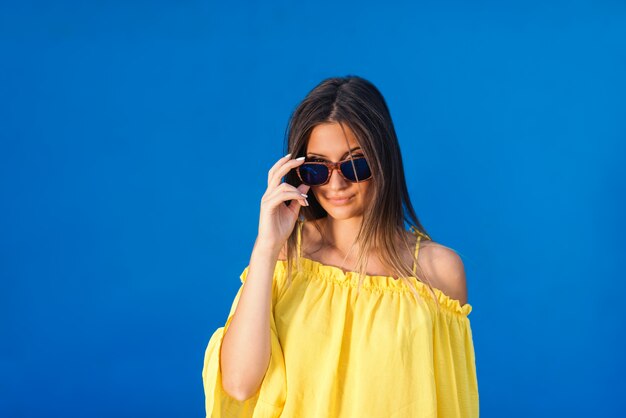 Portrait de sourire magnifique brune en chemisier jaune posant avec des lunettes de soleil