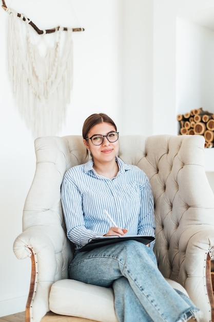 Portrait de sourire psychologue femme caucasienne assis dans un fauteuil sur le lieu de travail, tenant un dossier avec des papiers pour les notes.