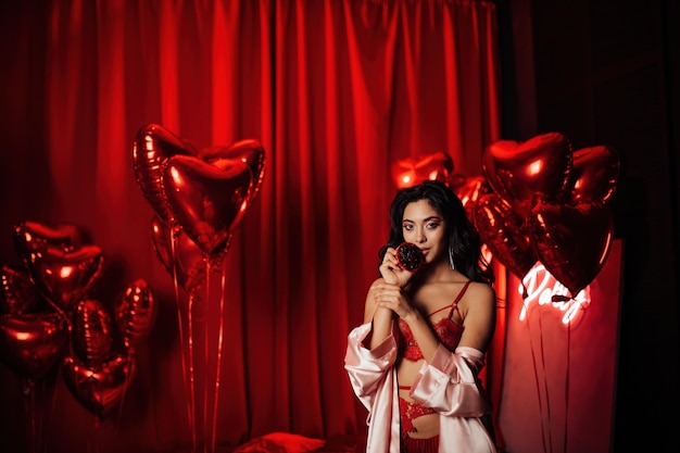 Portrait de sourire sexy fille asiatique glam maquillage en lingerie avec cupcake parmi les ballons rouges brillants