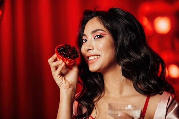 Portrait de sourire sexy fille asiatique glam maquillage en lingerie rouge avec cupcake et verre de champagne