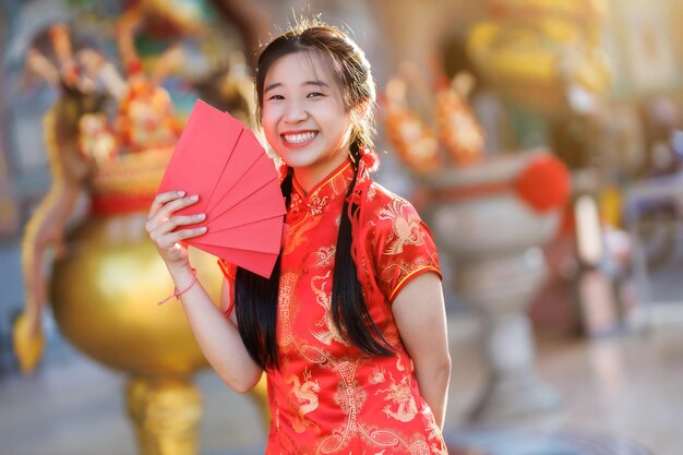 Portrait sourit jeune femme asiatique vêtue d'une robe cheongsam rouge tenant des enveloppes rouges décoration pour le festival du nouvel an chinois célébrer la culture de la chine au sanctuaire chinois Lieux publics en Thaïlande