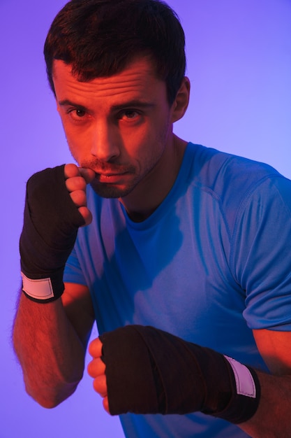 Portrait d'un sportif confiant en forme faisant des exercices de boxe isolés sur un mur violet