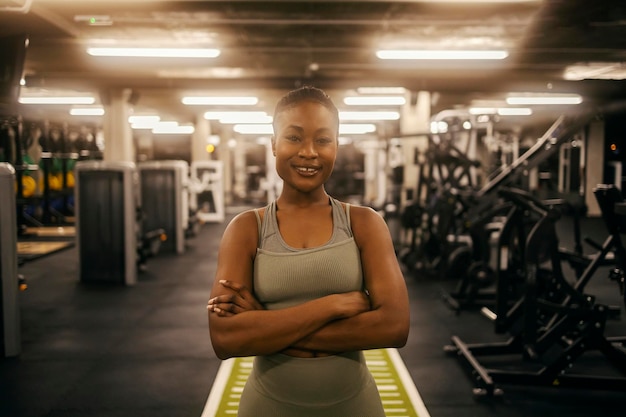 Portrait d'une sportive afro-américaine en forme debout avec les bras croisés au gymnase