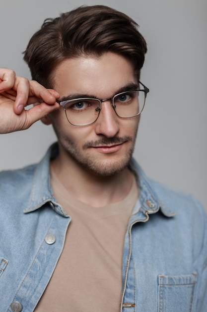 Portrait en studio d'un beau mec hipster à la mode avec une coiffure en denim décontracté à la mode portant des lunettes de soleil de mode vintage sur un fond gris neutre