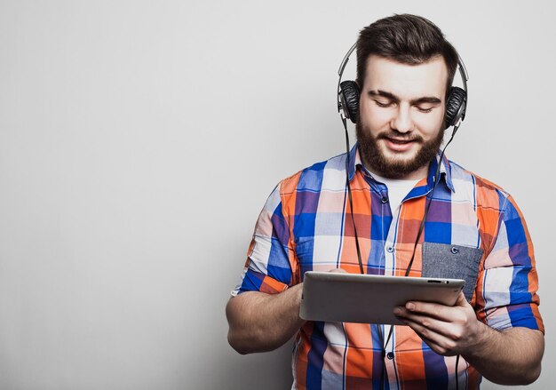 Portrait en studio d'un bel homme barbu à l'aide d'une tablette avec un casque sur un fond gris clair