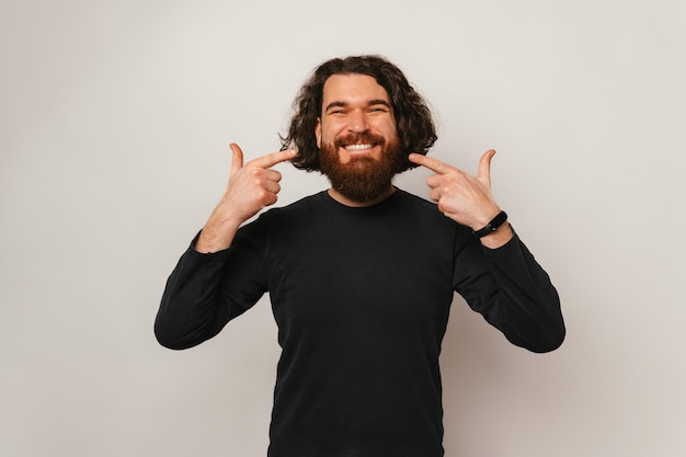 Portrait en studio d'un bel homme barbu pointant sur son sourire à pleines dents