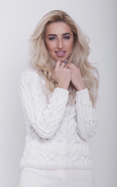 Portrait en studio de la belle femme blonde aux cheveux longs en pull chaud sur fond blanc