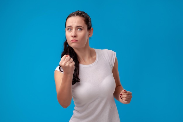 Portrait en studio d'une belle jeune femme vêtue d'un t-shirt blanc sur fond de mur bleu. Les gens émotions sincères.