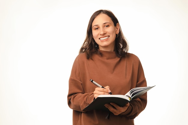 Portrait en studio sur blanc d'une femme souriante intelligente tenant un journal et un stylo