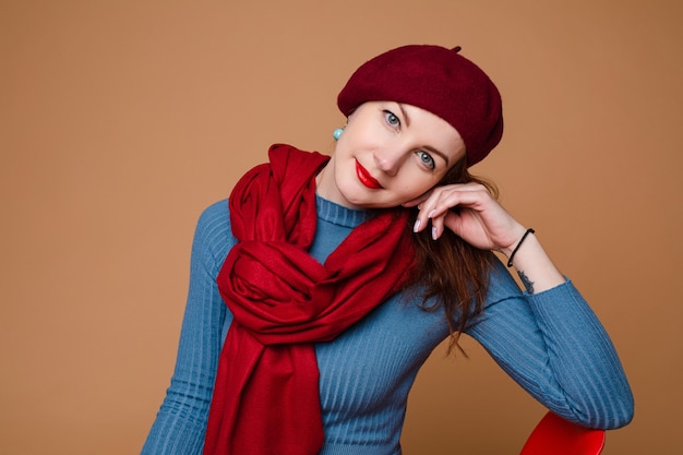 Portrait en studio d'une charmante dame portant un béret rouge et une écharpe sur une robe bleue légèrement souriante...