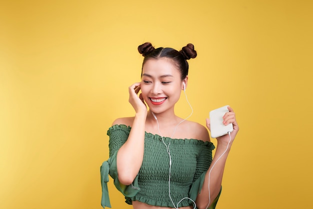 Portrait en studio coloré d'une jeune femme asiatique heureuse avec des écouteurs danse et chante.