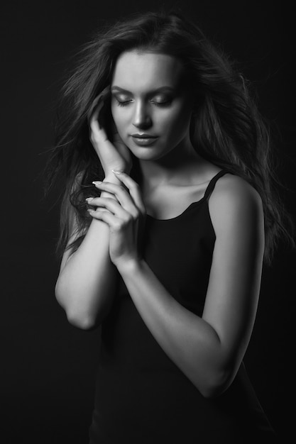 Portrait de studio dramatique d'une femme brune sensuelle avec un maquillage et une coiffure parfaits porte une robe noire classique posant dans un studio sombre. Prise de vue en noir et blanc