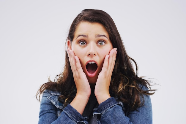 Portrait en studio éberlué d'une jolie jeune femme semblant choquée sur un fond gris