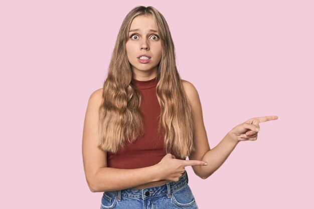 Photo portrait en studio d'une femme blanche blonde choquée pointant avec l'index vers un espace de copie