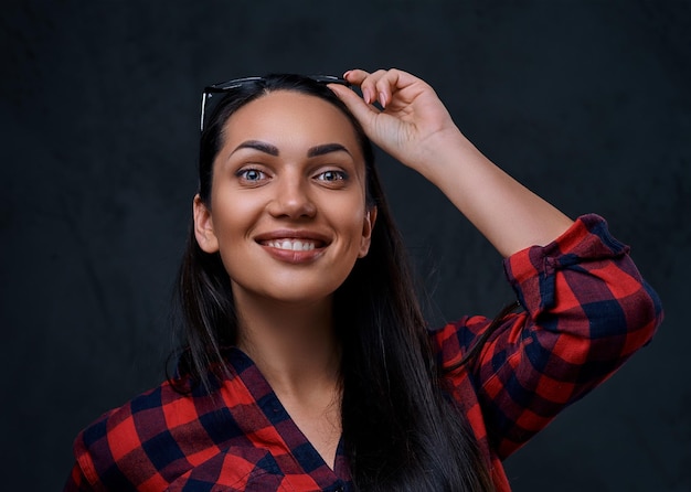 Portrait en studio d'une femme brune à lunettes vêtue d'une chemise rouge sur fond gris.