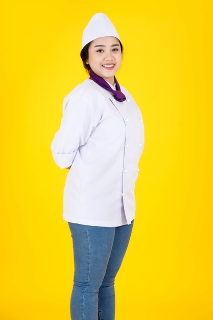 Portrait en studio d'une femme chef exécutive professionnelle asiatique réussie et confiante du restaurant de l'hôtel en uniforme de cuisine blanc debout souriant regardant la caméra les bras croisés sur fond jaune.