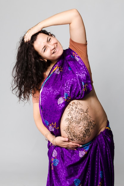 Portrait en studio d'une femme enceinte heureuse en sari indien, un ventre de femme enceinte peint au henné