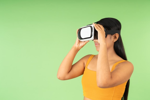 Photo portrait en studio avec un fond vert d'une femme hispanique ajustant les lunettes de réalité virtuelle qu'elle porte
