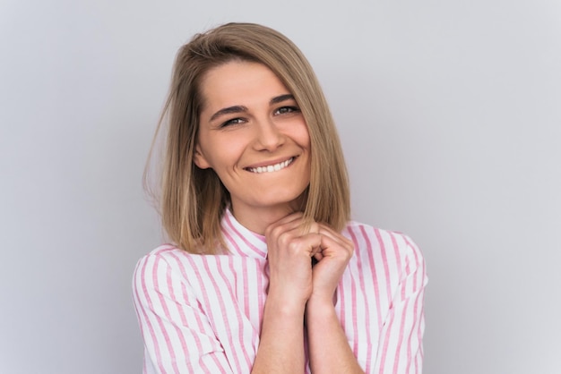 Portrait en studio de gaie et belle jeune femme blonde portant une chemise rose décontractée souriante et l'air heureuse Jolie femme brune positive avec des dents blanches en bonne santé sourire isolé sur mur blanc