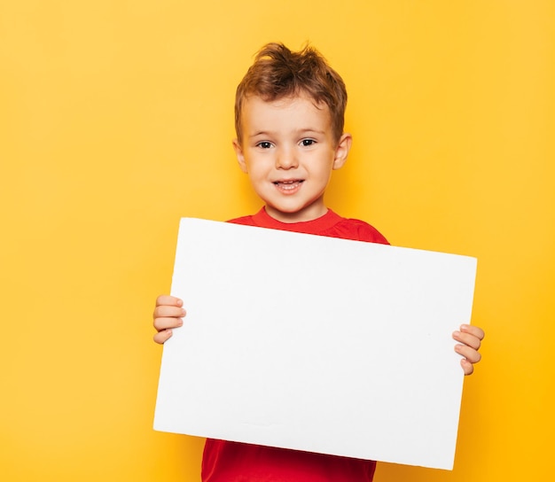 Portrait en studio d'un garçon heureux avec une affiche blanche propre dans ses mains sur un fond jaune vif avec une place pour votre texte ou votre publicité