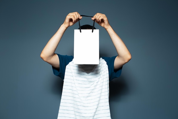 Portrait en studio d'un gars tenant un sac réutilisable blanc sur le visage sur fond bleu