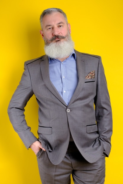 Portrait en studio homme barbu mature en costume gris à la recherche d'appareil photo, mode de vie de profession de travail, fond jaune.