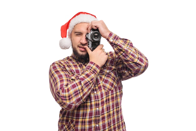 Portrait en studio d'homme barbu portant bonnet de Noel tenant un appareil photo rétro, faisant une photo. Fond blanc isolé