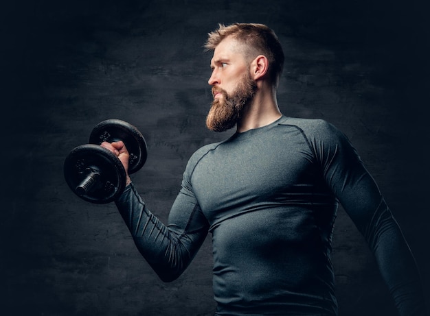 Portrait en studio d'un homme barbu sportif vêtu d'un vêtement de sport gris tenant une haltère.