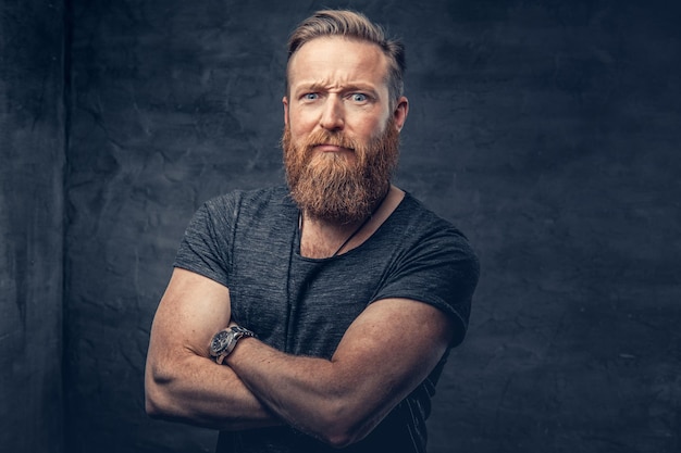 Portrait en studio d'homme hipster barbu rousse avec les bras croisés sur fond gris.