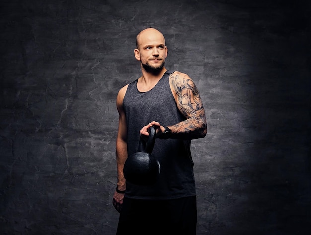 Portrait en studio d'un homme à tête rasée tatoué sportif tenant Kettlebell.