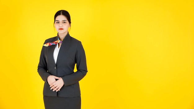 Portrait en studio d'une hôtesse de l'air d'une hôtesse de l'air féminine intelligente et confiante en costume d'uniforme formel avec une écharpe debout souriante regardant la caméra posant sur fond jaune.