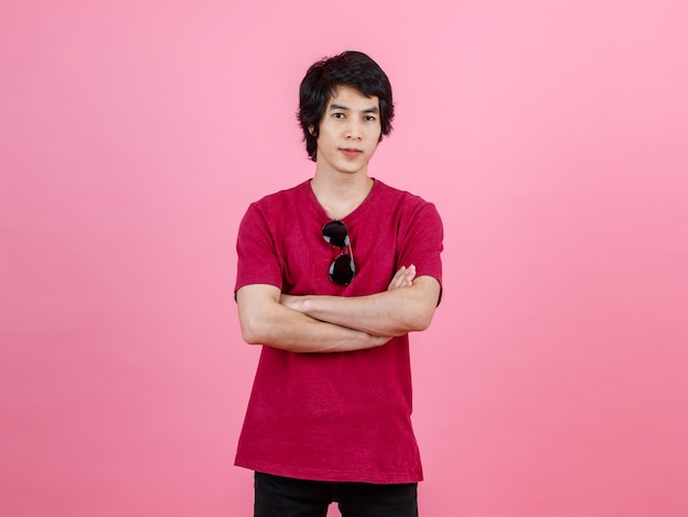 Portrait en studio d'un jeune adolescent urbain asiatique modèle masculin de mode en tenue de rue décontractée t-shirt et jeans noirs avec des lunettes de soleil aviateur debout posant regarder la caméra sur fond rose