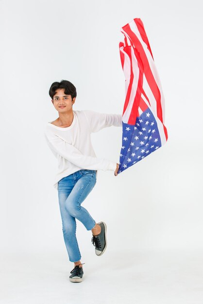 Portrait en studio d'un jeune asiatique LGBT gay bisexuel homosexuel masculin modèle à la mode en tenue décontractée et lunettes de soleil de mode debout tenant en agitant le drapeau national des États-Unis sur fond blanc