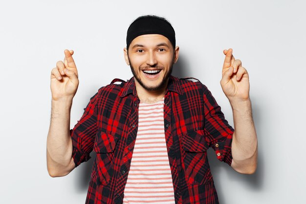 Portrait en studio de jeune bel homme heureux avec les doigts croisés portant une chemise à carreaux rouge