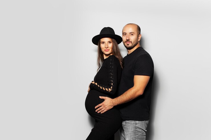 Photo portrait en studio d'un jeune couple futurs parents mari étreignant sa femme sur fond blanc vêtu de noir
