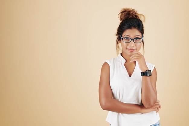 Portrait en studio d'une jeune femme asiatique positive dans des verres debout sur fond beige