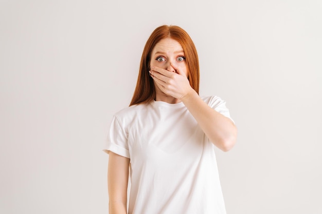 Portrait en studio d'une jeune femme choquée et étonnée couvrant la bouche avec des paumes pressées qui sautent les yeux à