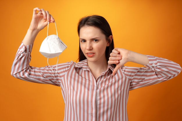 Portrait en studio d'une jeune femme enlevant son masque facial sur fond jaune