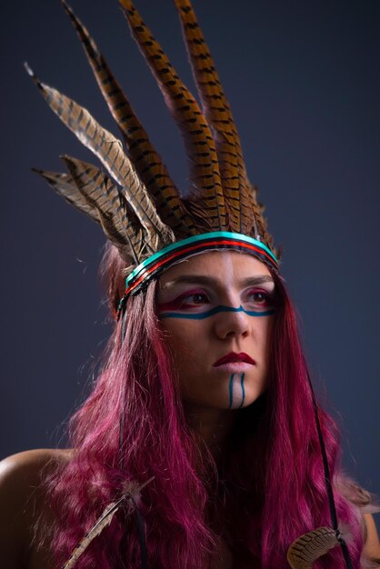 Portrait en studio d'une jeune fille en pacahontas avec plumes, sur fond gris.