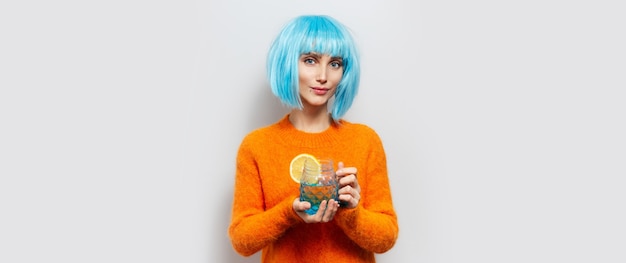 Portrait en studio de jeune fille avec perruque bleue, tenant un verre d'eau citronnée.