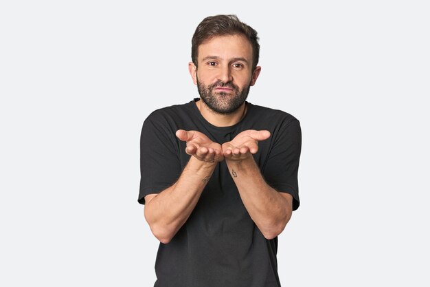 Portrait en studio d'un jeune homme hispanique pliant les lèvres et tenant les paumes pour envoyer un baiser en l'air