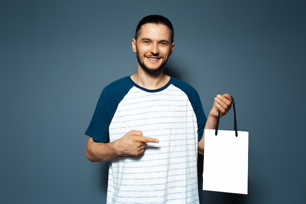 Portrait en studio d'un jeune homme souriant pointant vers le sac réutilisable blanc