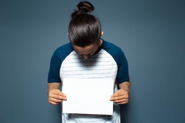 Portrait en studio de jeune homme tenant un carton blanc vide sur fond de couleur bleue