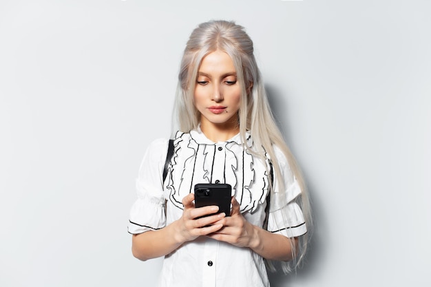 Portrait en studio de jeune jolie fille blonde à l'aide d'un smartphone envoyant un message sur fond blanc