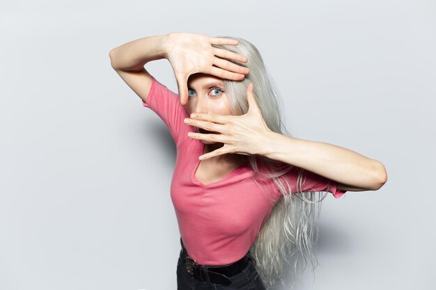 Portrait en studio de jeune jolie fille blonde faisant un cadre de signe photo avec les mains sur fond blanc