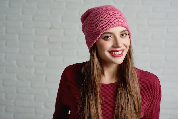 Portrait en studio d&#39;un jeune mannequin souriant, coiffé d&#39;un bonnet rose et d&#39;un sweat-shirt rouge.