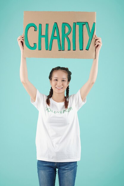 Portrait en studio d'une jeune volontaire asiatique heureuse tenant une pancarte de charité au-dessus de sa tête et souriant à la caméra