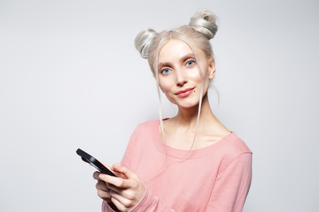 Portrait en studio de jolie fille avec des petits pains à l'aide d'un smartphone sur un mur blanc