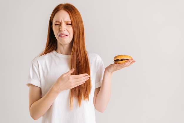 Portrait en studio d'une jolie jeune femme insatisfaite avec dégoût pointant vers le hamburger les yeux fermés