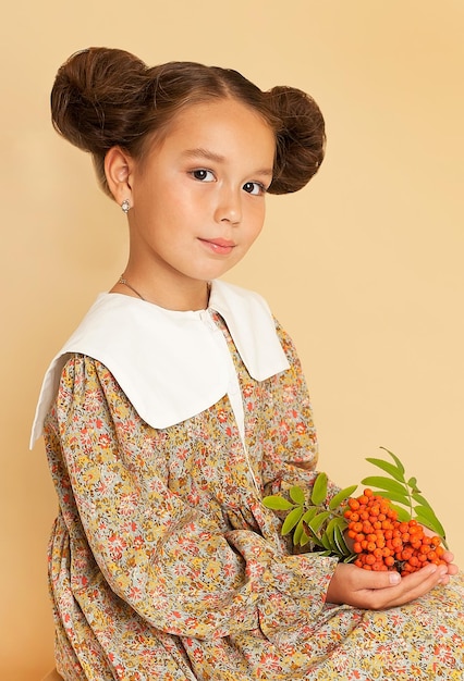 Portrait en studio d'une jolie petite fille avec des baies de sorbier dans les mains et deux touffes de cheveux sur la tête. Portrait artistique d'enfants. Photographie d'art.
